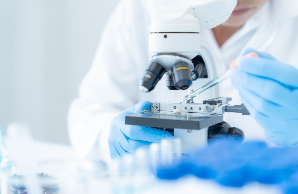 A person in a lab coat examines an object with a focused expression in a laboratory setting.